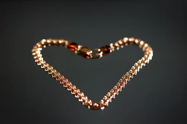 Gold bracelet in the shape of a heart on a gray background