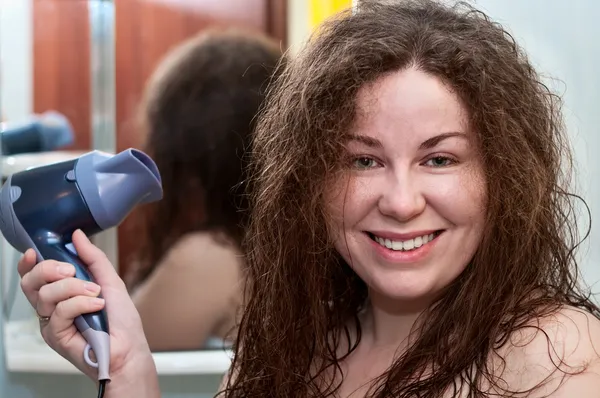 Young caucasian woman with curly brown bushy hair holding hairdryer by 