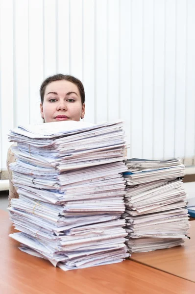 Head of young caucasian woman behind pile from project drawings blueprints