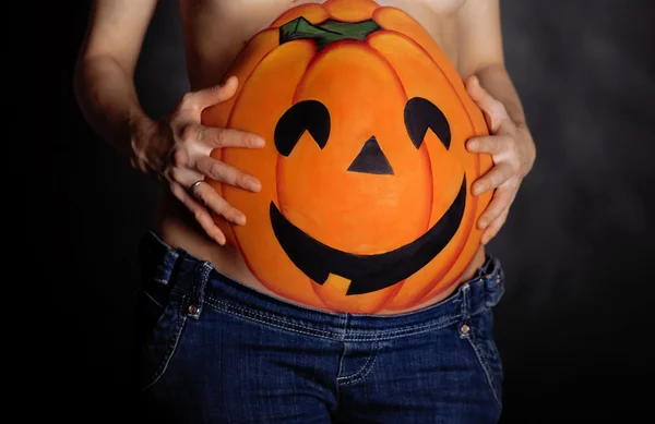 Halloween pumpkin painted on belly of pregnant