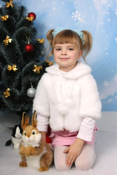 Little girl in a white coat with a rabbit around a Christmas tre