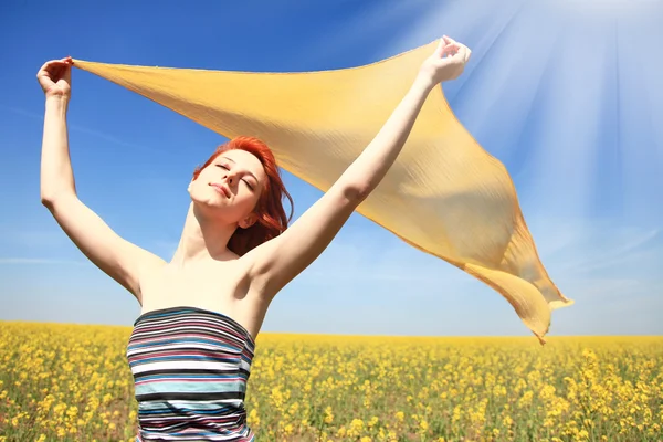 Young woman with open arms keep yellow silk on wind at rape field. Shine fr