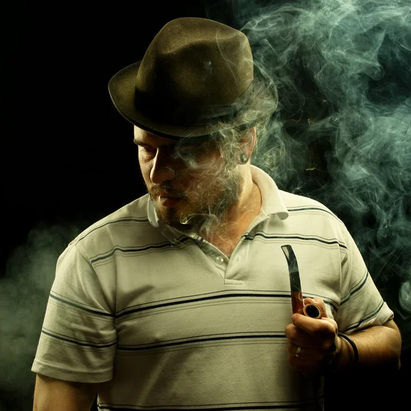 Dark fine art portrait of a smoking man in hat. With tobacco pip