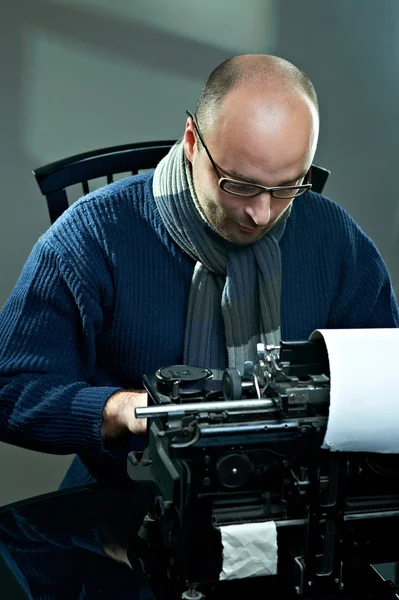 Old fashioned bald writer in glasses writing book on a vintage typewriter