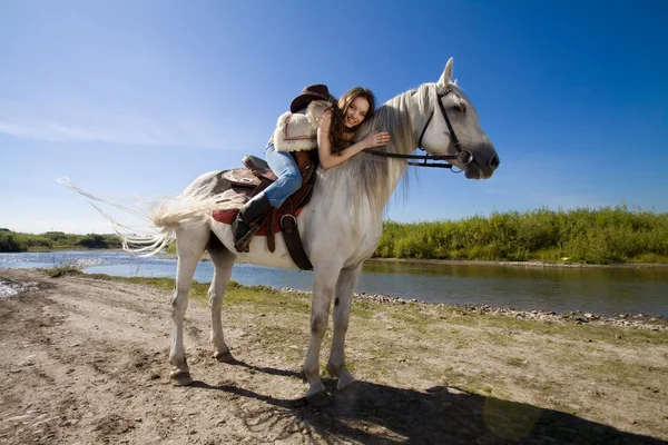 Young cowgirl on white horse at the rural river