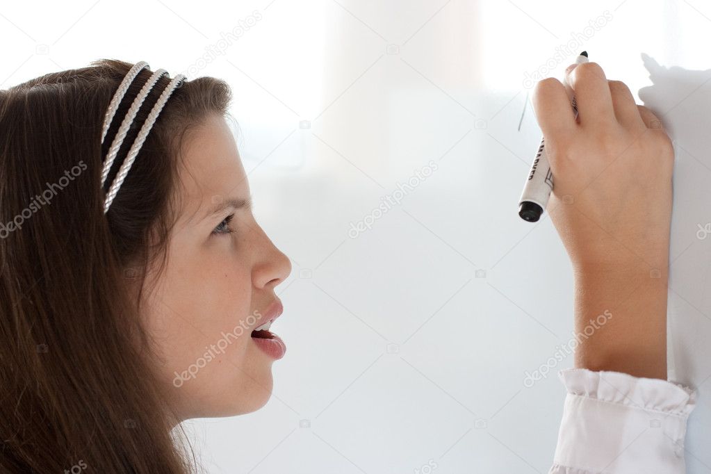 Cute preteen schoolgirl writing letter on whiteboard studiously