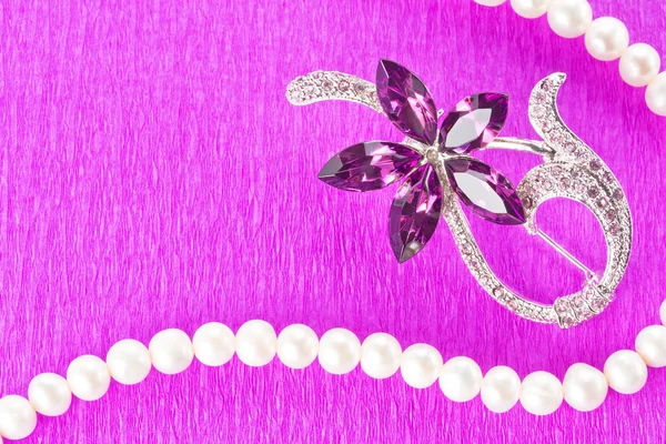 Brooch and pearl necklace on purple background