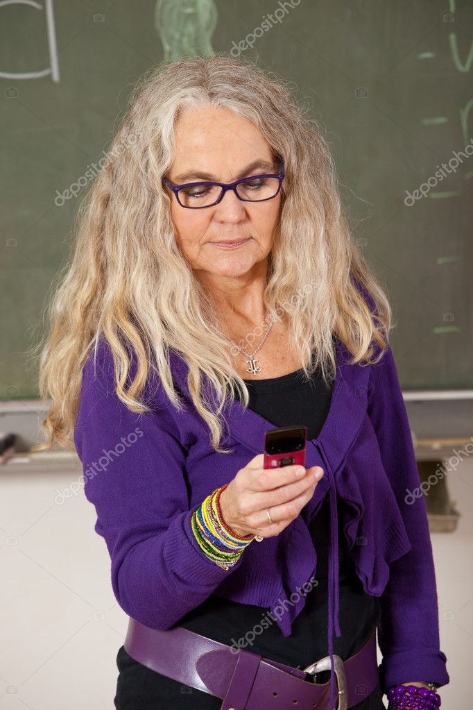Mature teacher standing in the classroom sending a text message