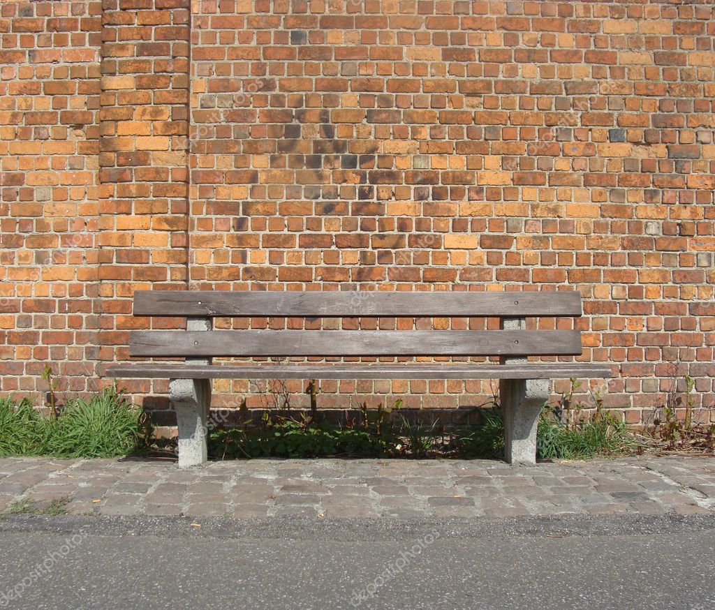 Wooden bench with path in front of a brick wall - Stock Image