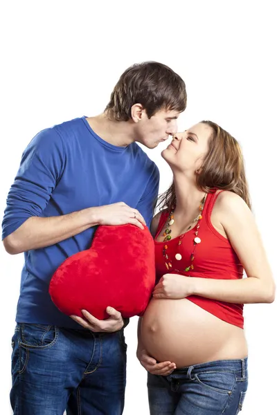 Happy joking couple embracing pregnant belly and red heart