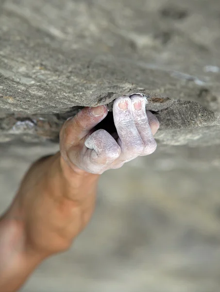 Rock climber's hand grasping handhold on natural cliff. His hand is covered in chalk. Shallow depth of field.