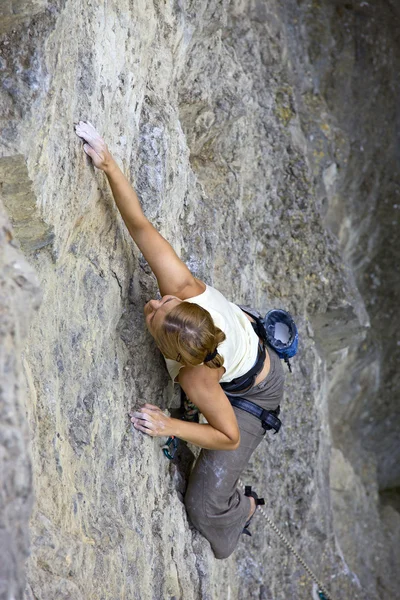 Female rock climber clinging to a cliff as she battles her way up