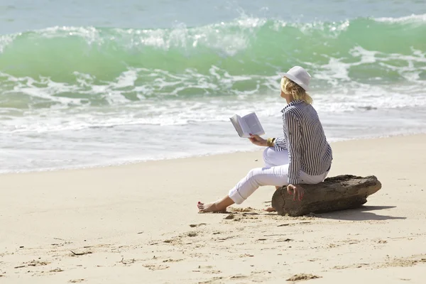 Woman with book is sitting on a stump by the wave line