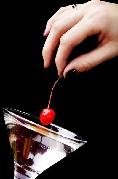 The hand putting the red cherry to the martini glass