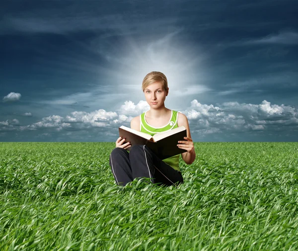 College girl reading big book in green grass