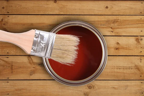 Red paint can with brush on wooden floor