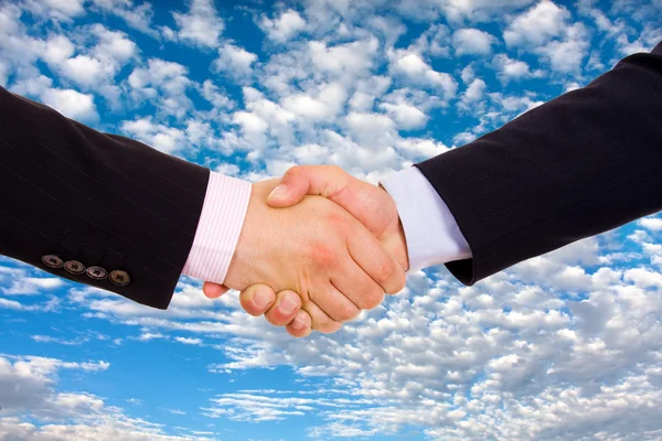 Business men hand shake over a blue sky with clouds as backgroun