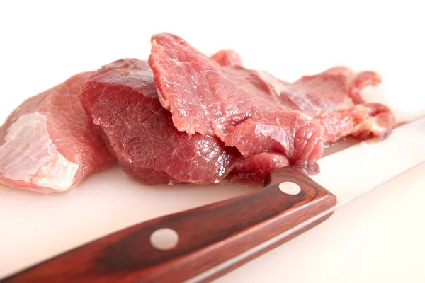 Sliced ​​meat and a sharp knife on a white cutting board