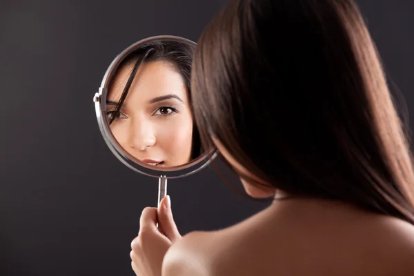 A beauty image of a young woman looking into a mirror, smiling.