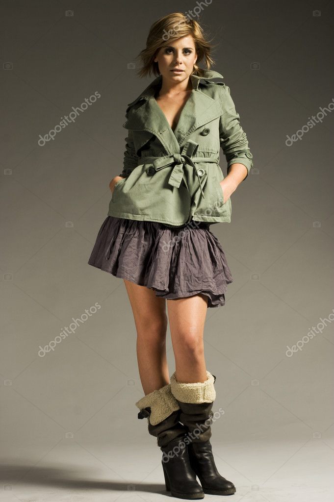 Beautiful blonde girl wearing green coat and mini skirt on grey background