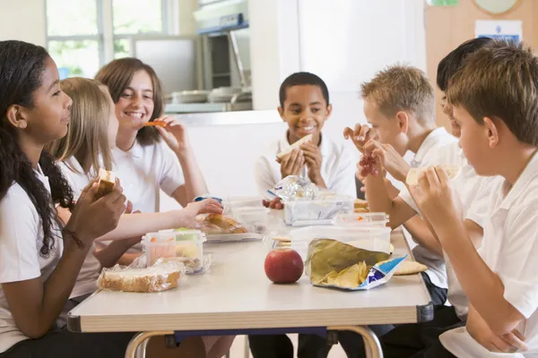 A group of cheerful small school kids in canteen, eating lunch and talking.  stock photo