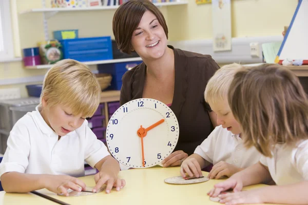 Teacher helping schoolchildren learn to tell time in primary cla