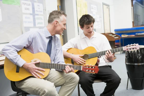 Schoolboy and teacher playing guitar in music class
