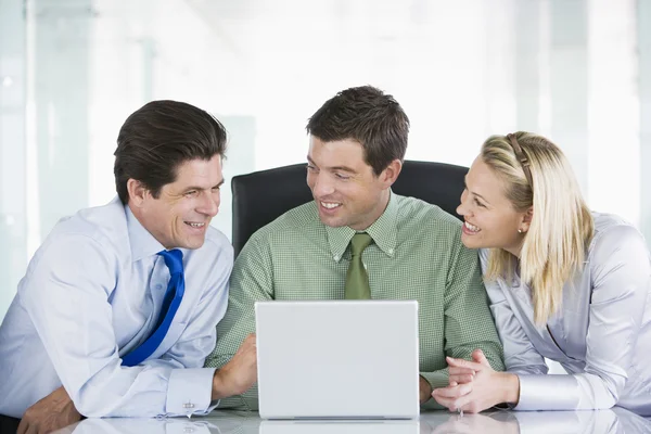 Three businesspeople in a boardroom looking at laptop smiling