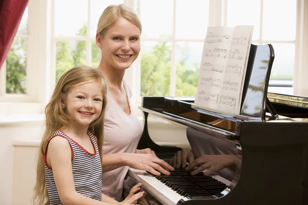 Woman and young girl playing piano and smiling