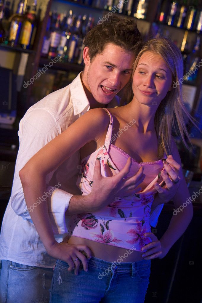 Young man in a nightclub grabbing young women's breasts from beh