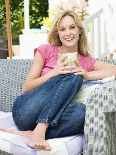 Woman sitting outdoors on patio with coffee smiling