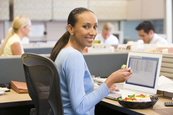 Businesswoman in cubicle with laptop eating salad