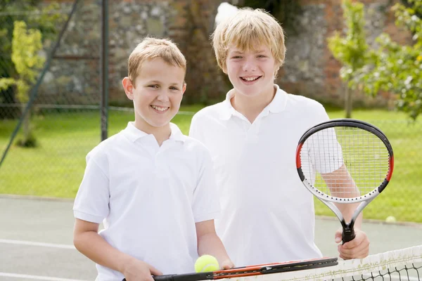 Two young male friends with rackets on tennis court smiling — Stock Photo #4780032