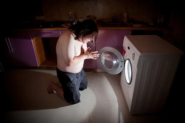 Asian fat man kneel in prayer by washing machine by Marina Pissarova Stock 