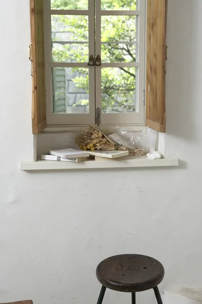 Books and dried flowers on window sill, wooden stool below