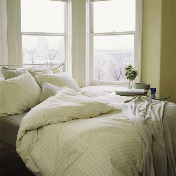 Bed with linens, comforter beside window