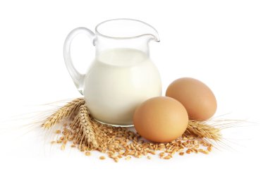 Glass jug with milk, wheat seeds and two eggs on white background clipart