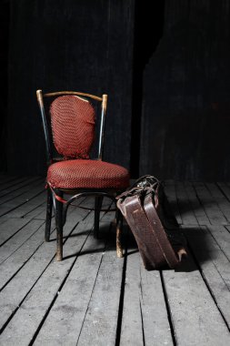 Old fashioned chair and well-traveled vintage suitcase on wooden floor clipart