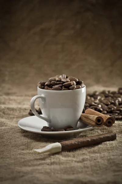 Pohár s kávová zrna a skořice na pytlovina — Stock fotografie