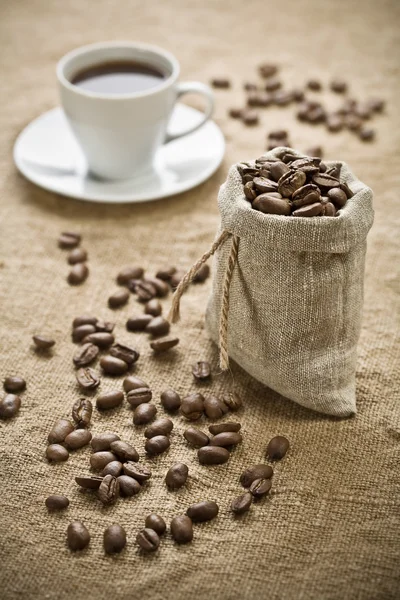 Coffee beans and cup of coffee on sacking — Stock Photo, Image