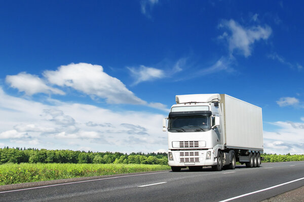 Белый грузовик на летнем шоссе под голубым небом
