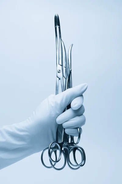 Mão de cirurgião com fórceps sobre azul — Fotografia de Stock