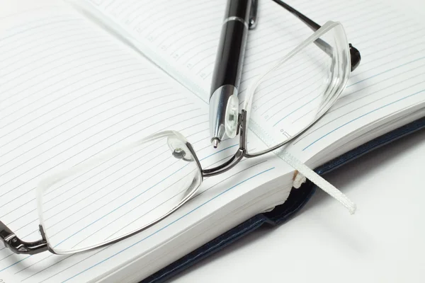 Diário de negócios aberto com caneta e óculos sobre fundo branco — Fotografia de Stock