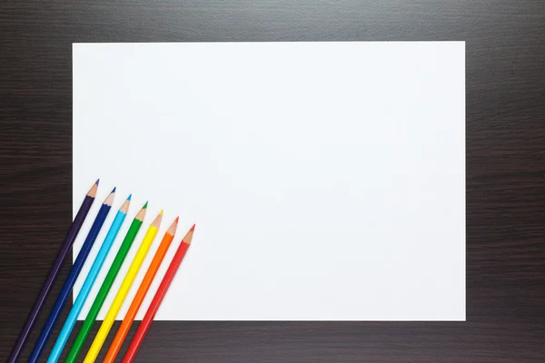 Hoja de papel en blanco sobre la mesa con lápices de colores — Foto de Stock