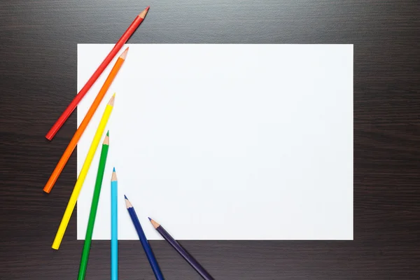 Hoja de papel en blanco sobre la mesa marrón con lápices de colores — Foto de Stock