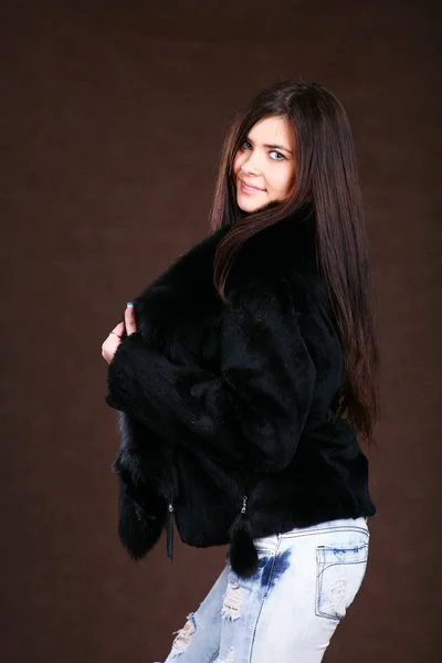 Attracive 年轻女子穿着一件裘皮大衣和棕色背景上牛仔裤 — 图库照片