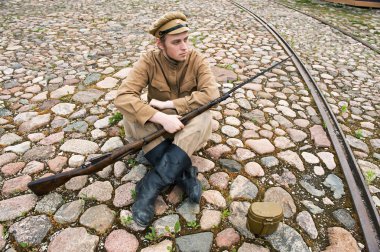 Soldier with gun and boiler in uniform of World War I, sit down and resting on the pavement. Costume accord the times of World War I. Photo made at cinema city clipart