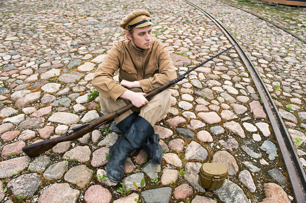 Soldier with gun and boiler in uniform of World War I, sit down and resting on the pavement. Costume accord the times of World War I. Photo made at cinema city