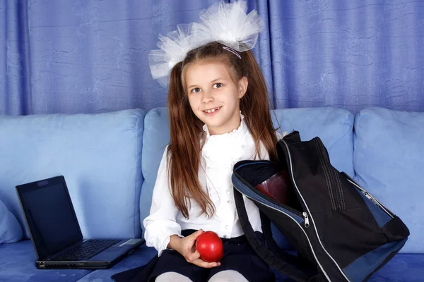 Skolflicka tjej med bärbara, ryggsäck och rött äpple i soffa — Stockfoto