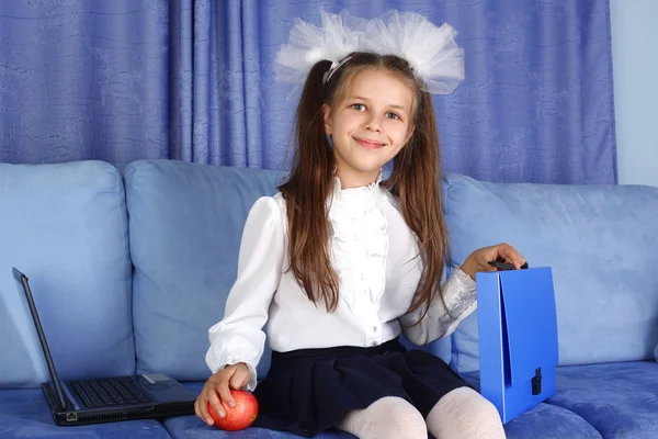 Школьная девочка с ноутбуком, рюкзаком и красным яблоком на диване — стоковое фото